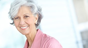 Lab tech creating wax version of dentures
Woman with gray hair in pink shirt smiling
