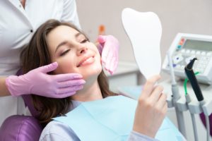 A woman with brown hair in a dentist chair looking in a mirror while a dentist with purple gloves stands behind her