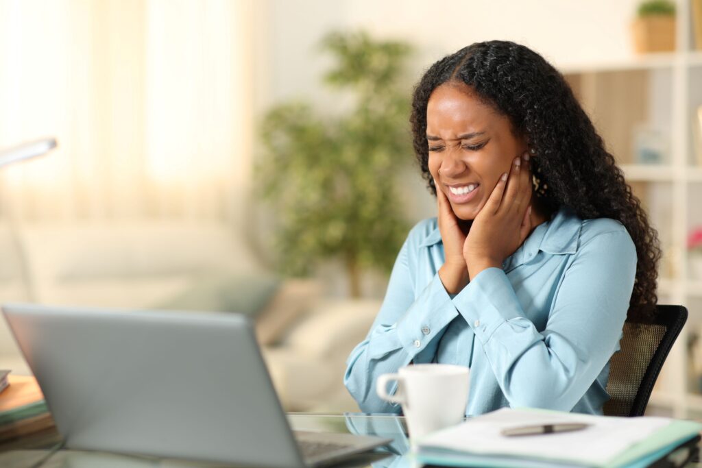 Woman sitting at laptop with eyes shut and fingers over jaw